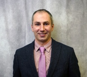 Eric wears a purple tie and a suit jacket